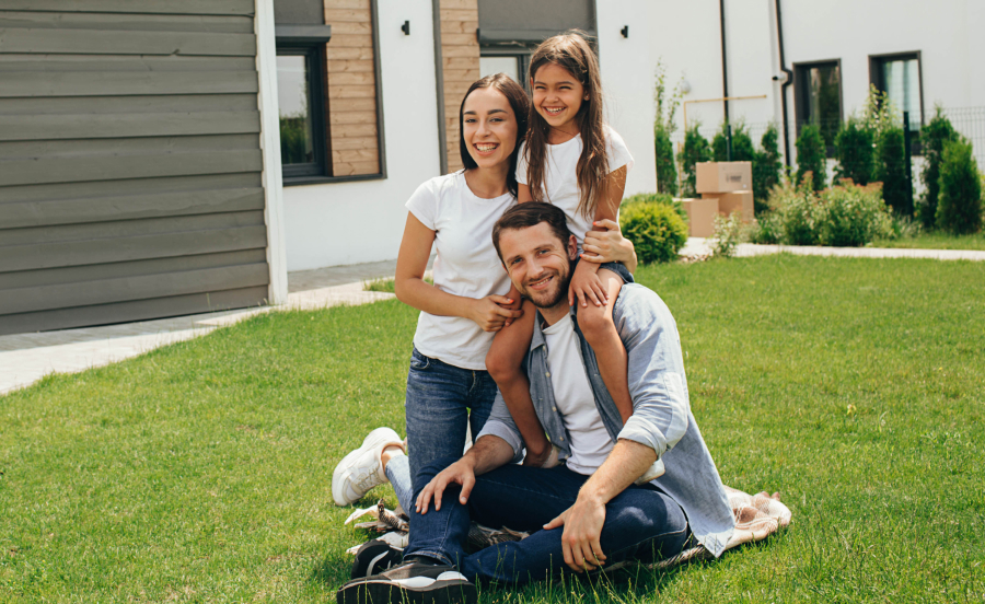 Imagen de una familia feliz frente a una casa moderna en la Zona Cantera, con árboles y un vecindario tranquilo al fondo, reflejando seguridad y bienestar familiar.